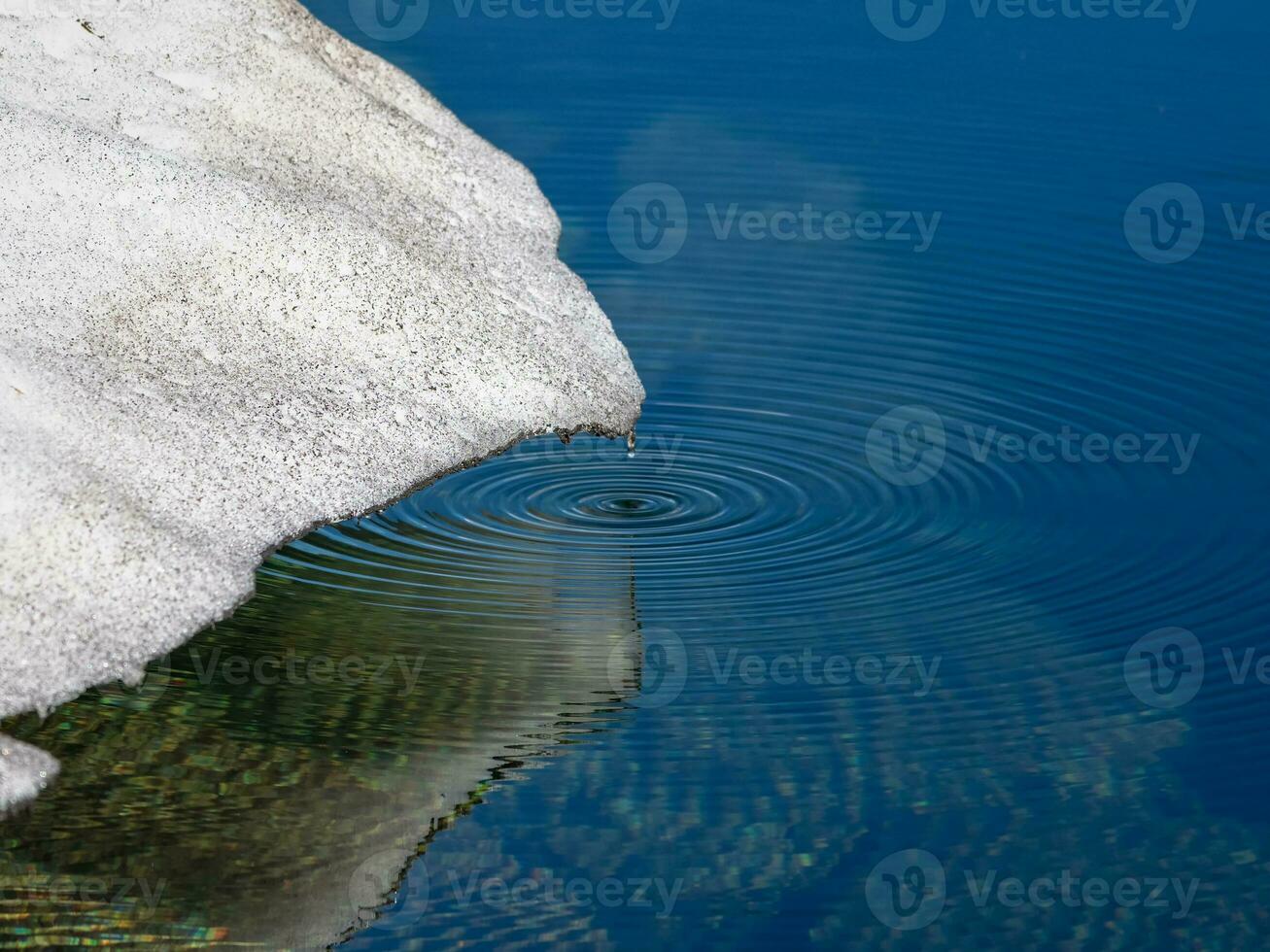 Round drops of water on the surface of a crystal mountain lake from the melting of a glacier. Water droplets fall on the surface of the water and splashing. Desktop laptop wallpaper. photo