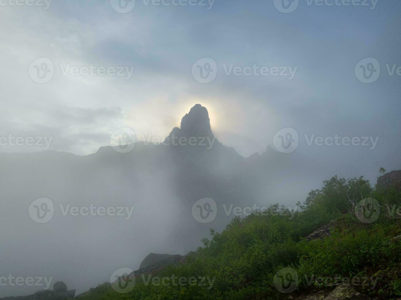 Morning sun behind the mountain peak, the dawn in the misty mountains. Atmospheric ghostly minimalism with large mountain tops in cloudy sky. West Sayans. photo