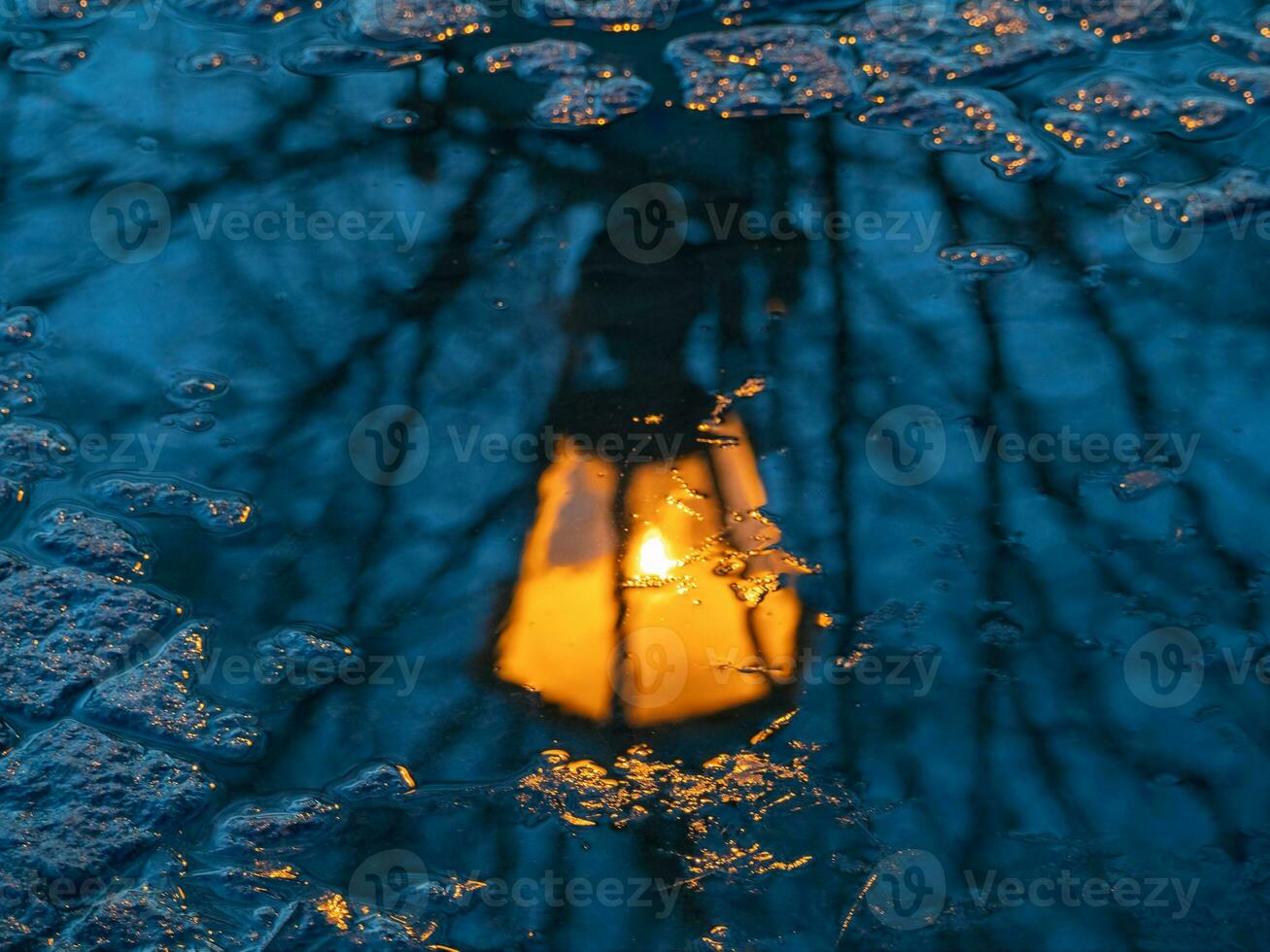 Blurred antique lantern shines yellow and is reflected in a spring puddle. Urban postcard abstract view. photo
