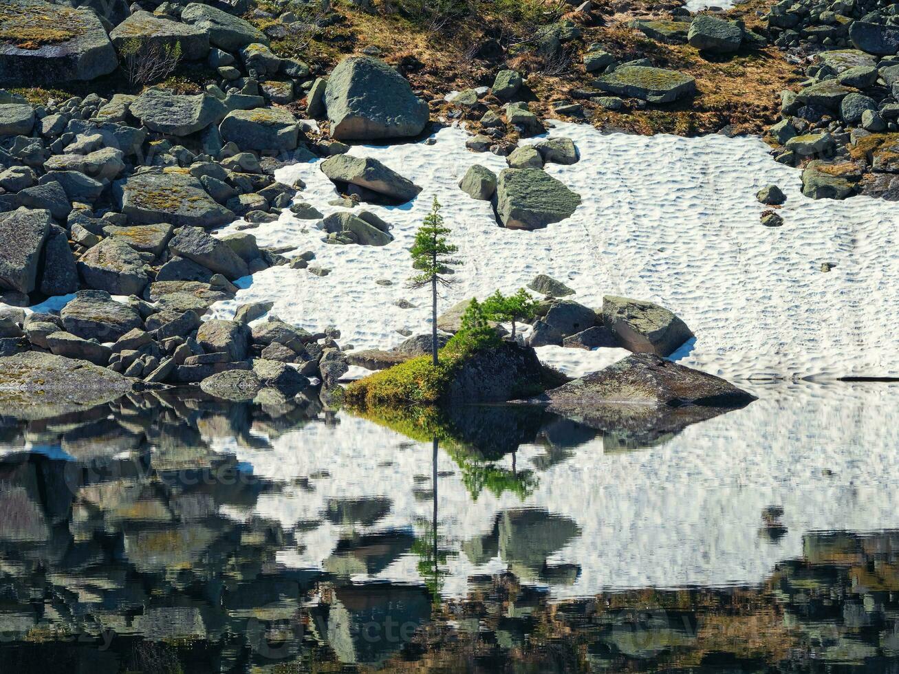 Rock in clear mountain lake. Snowy mountain reflected in azure clear water of glacial lake. Beautiful summer background with snow-white glacier reflection in water surface of mountain lake. photo