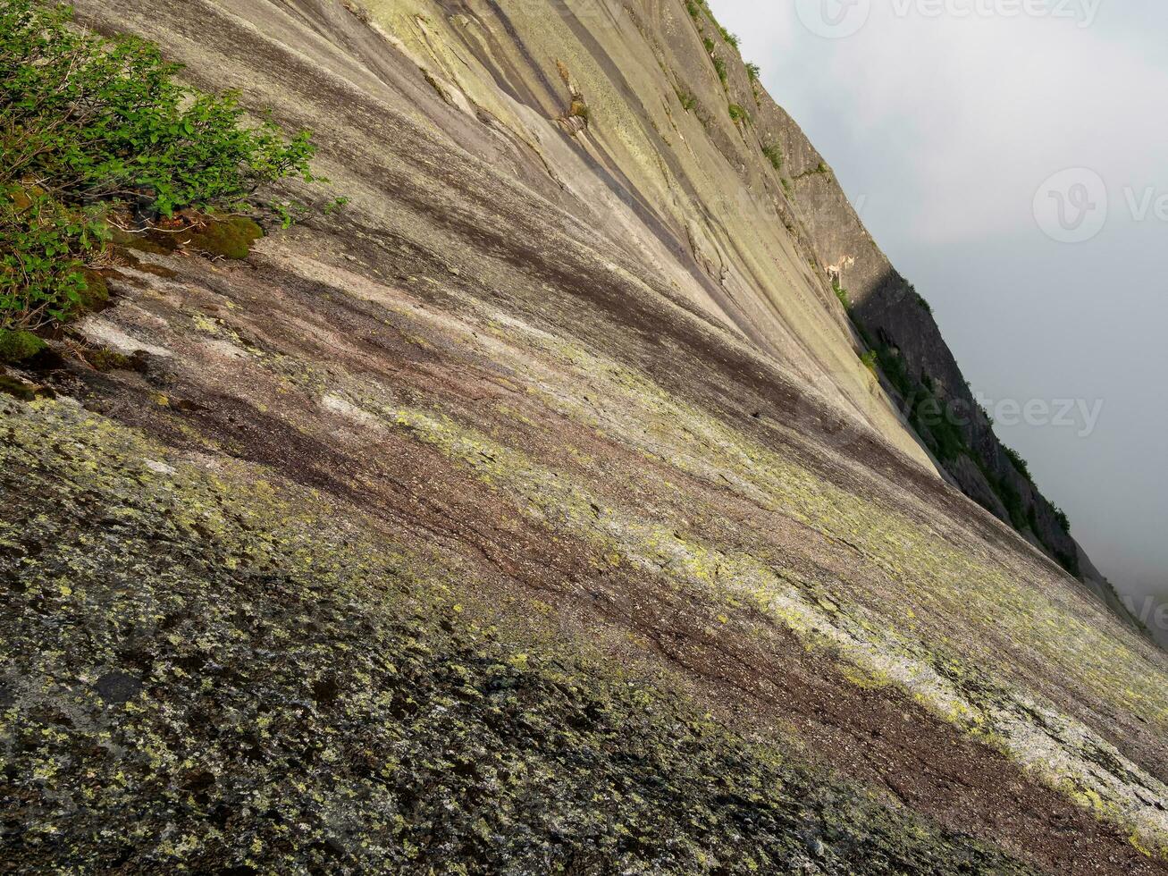 Steep textured granite mountain slope. Stone texture. Cross section of rocks. Geological layers. Colored layers of stones in section of the mount, different rock formations and soil layers. photo