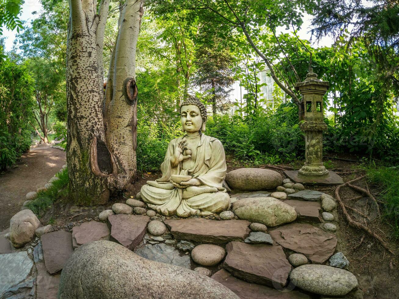 Stone Gautama Buddha decorative statue in a garden under green leaves. Outdoor Garden decor concept. Abakan photo