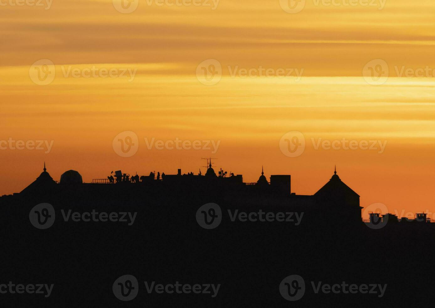 Contrasting view of dark silhouette of the roofs against the bright orange evening sky. Low angle view of long row of characteristic townhouses with roofs and chimneys of Europe houses during sunset photo