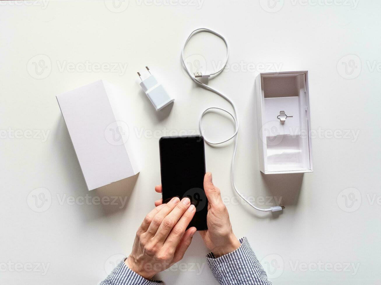 Unpacking a new smartphone on a white table. Female hands holding modern smartphone with blank screen. Online shopping concept. photo