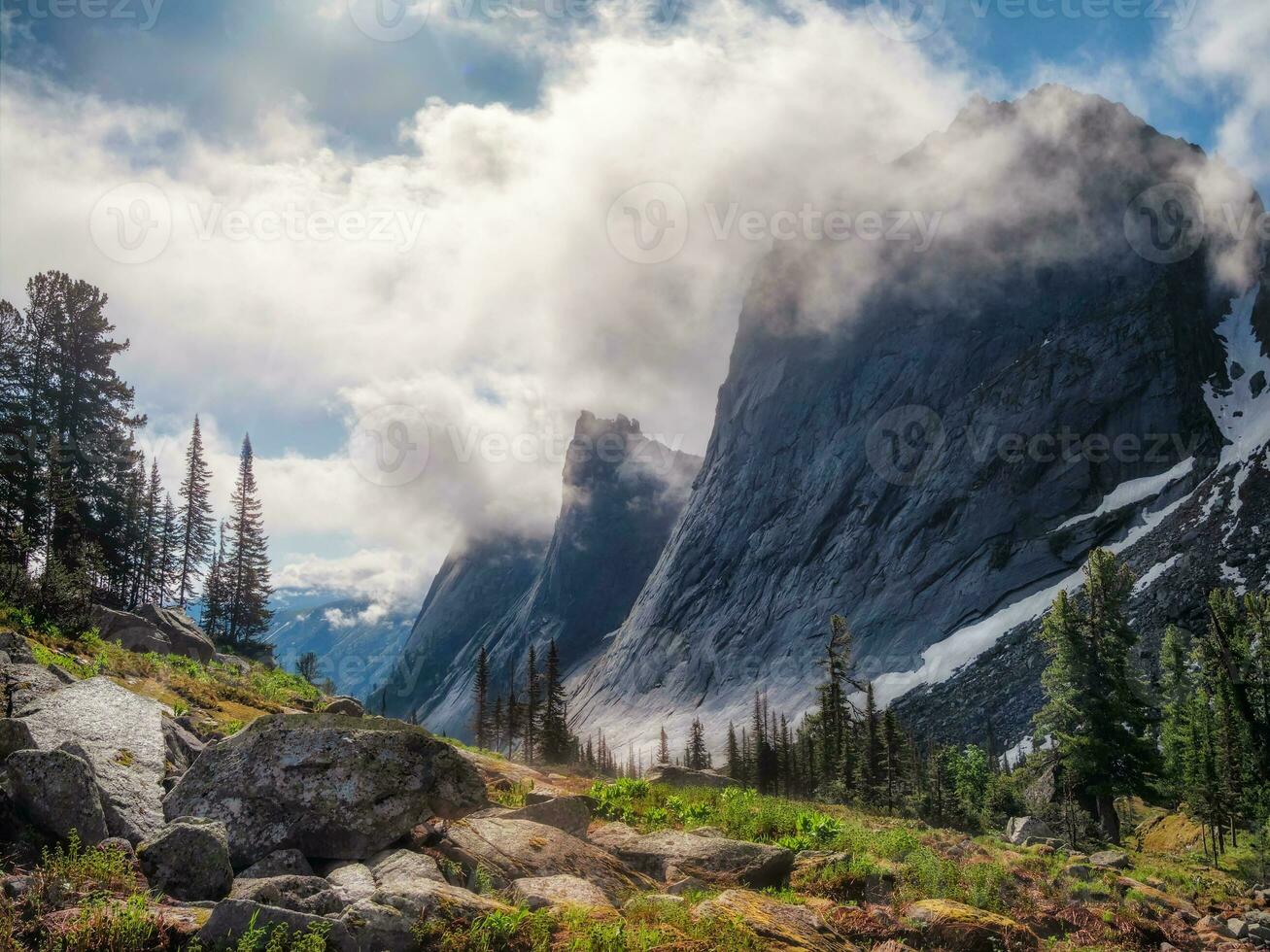 Misty mountain landscape with hills and rocks on background of mountain gorge in mist. Bright sunny morning atmospheric scenery with mountain relief in dark green valley in rainy weather. photo