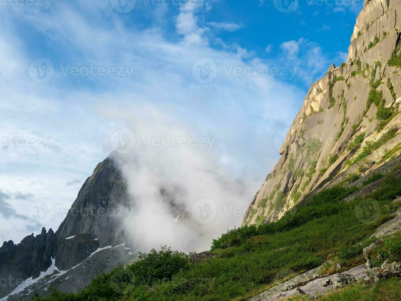 Sunrise in the mountains, in thick clouds. Light on the pass. The glacier is melting, illuminated by the bright golden morning sun. Fog on sunny slopes, natural majestic view. photo