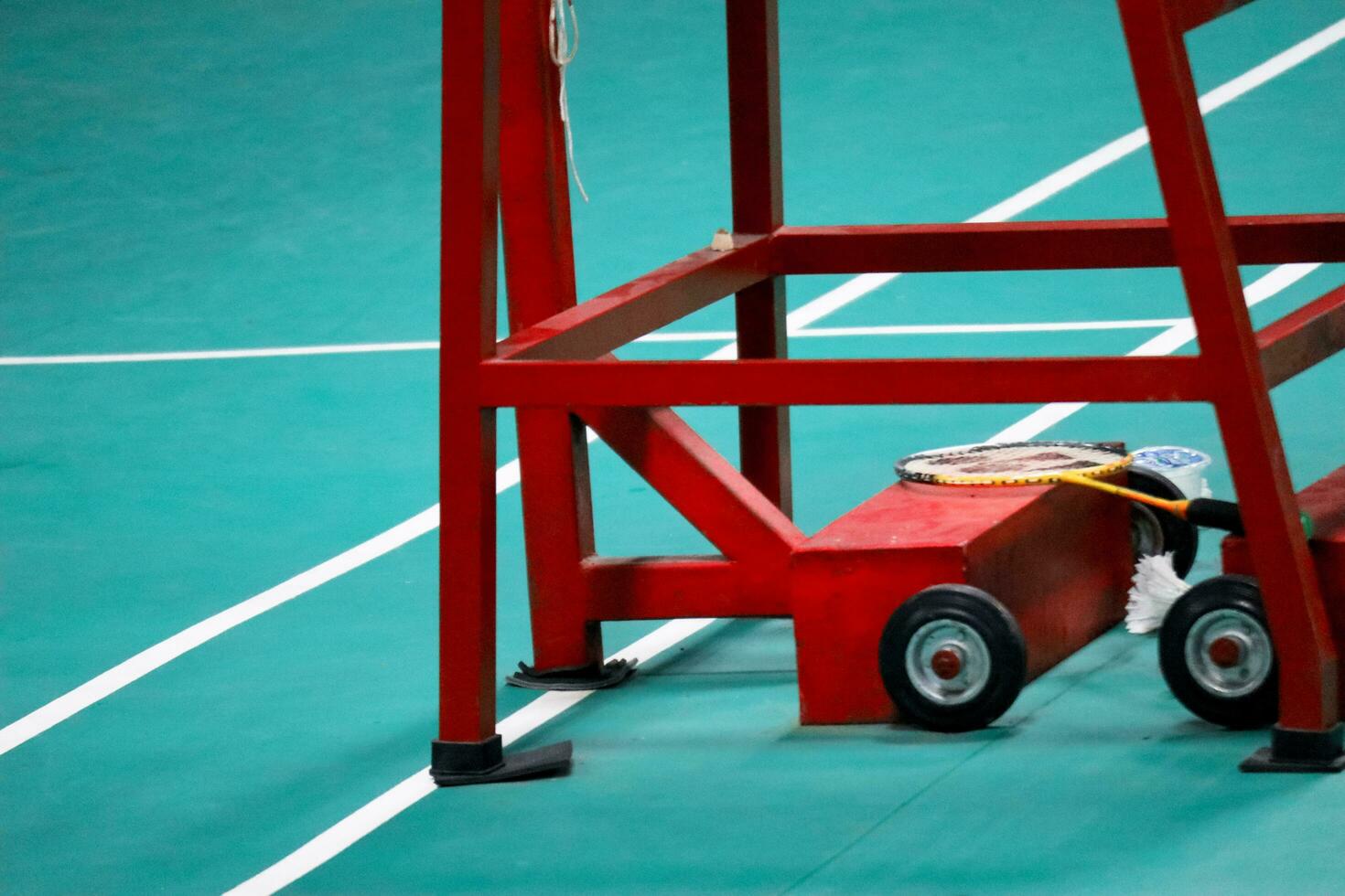 The badminton referee's chair is red with a green badminton court background photo