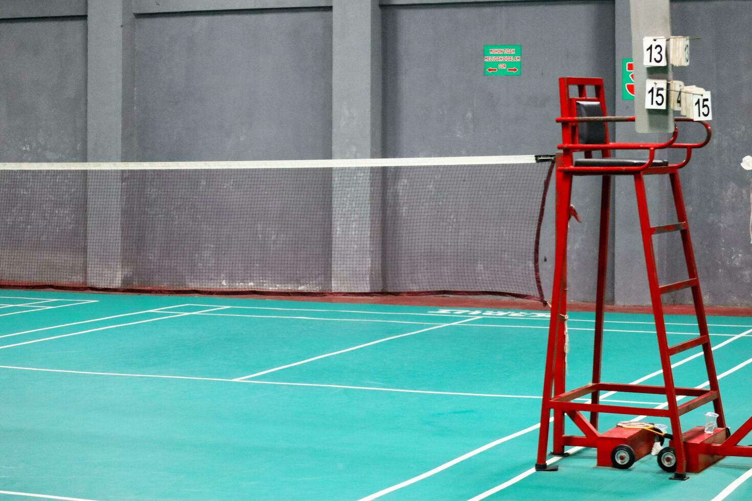 The badminton referee's chair is red with a green badminton court background photo