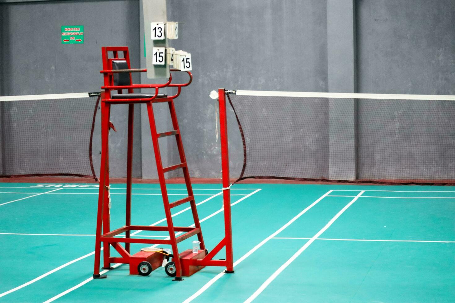 The badminton referee's chair is red with a green badminton court background photo
