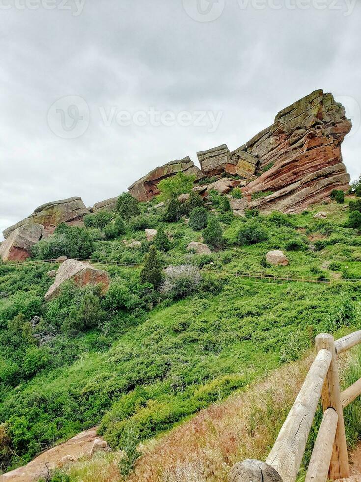 Rocks and wooden fence on a green hillside under a cloudy sky photo