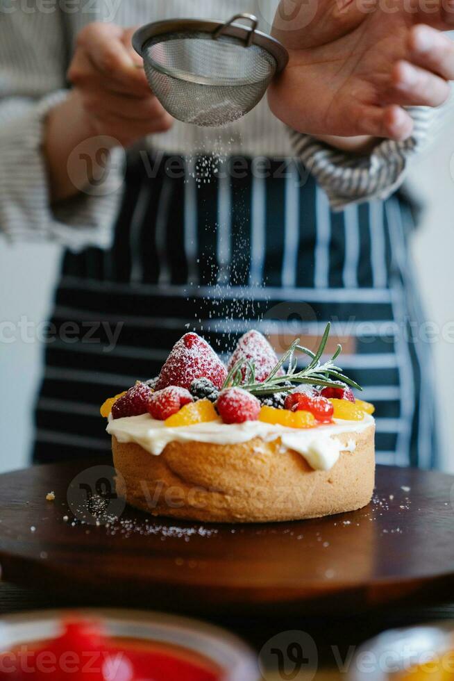 Chef sprinkling icing sugar on a fresh fruit tart with berries photo