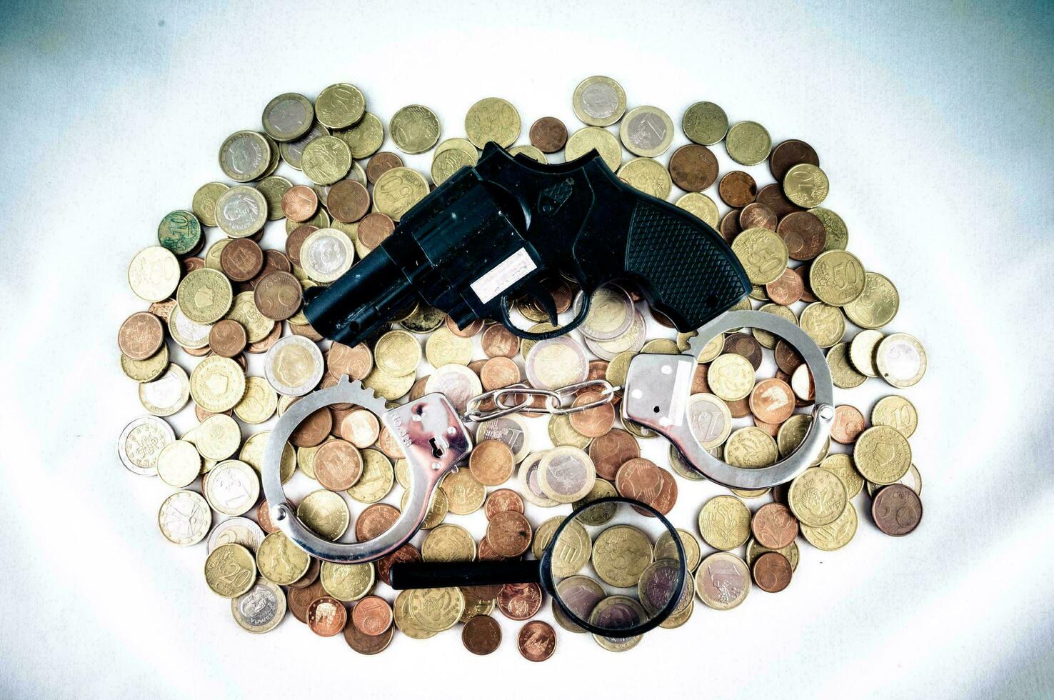 a gun, magnifying glass and handcuffs on a pile of coins photo