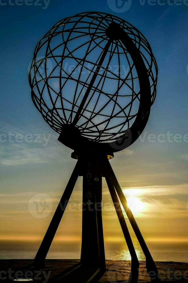 the sun sets behind a globe sculpture photo