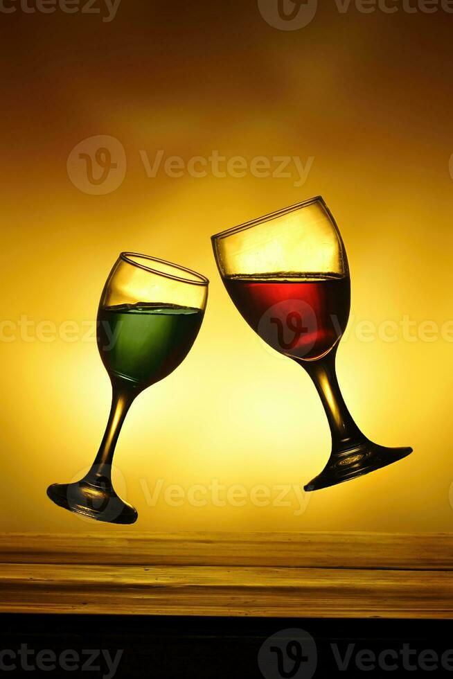 Two glasses of red and green wine on wooden table with golden light photo