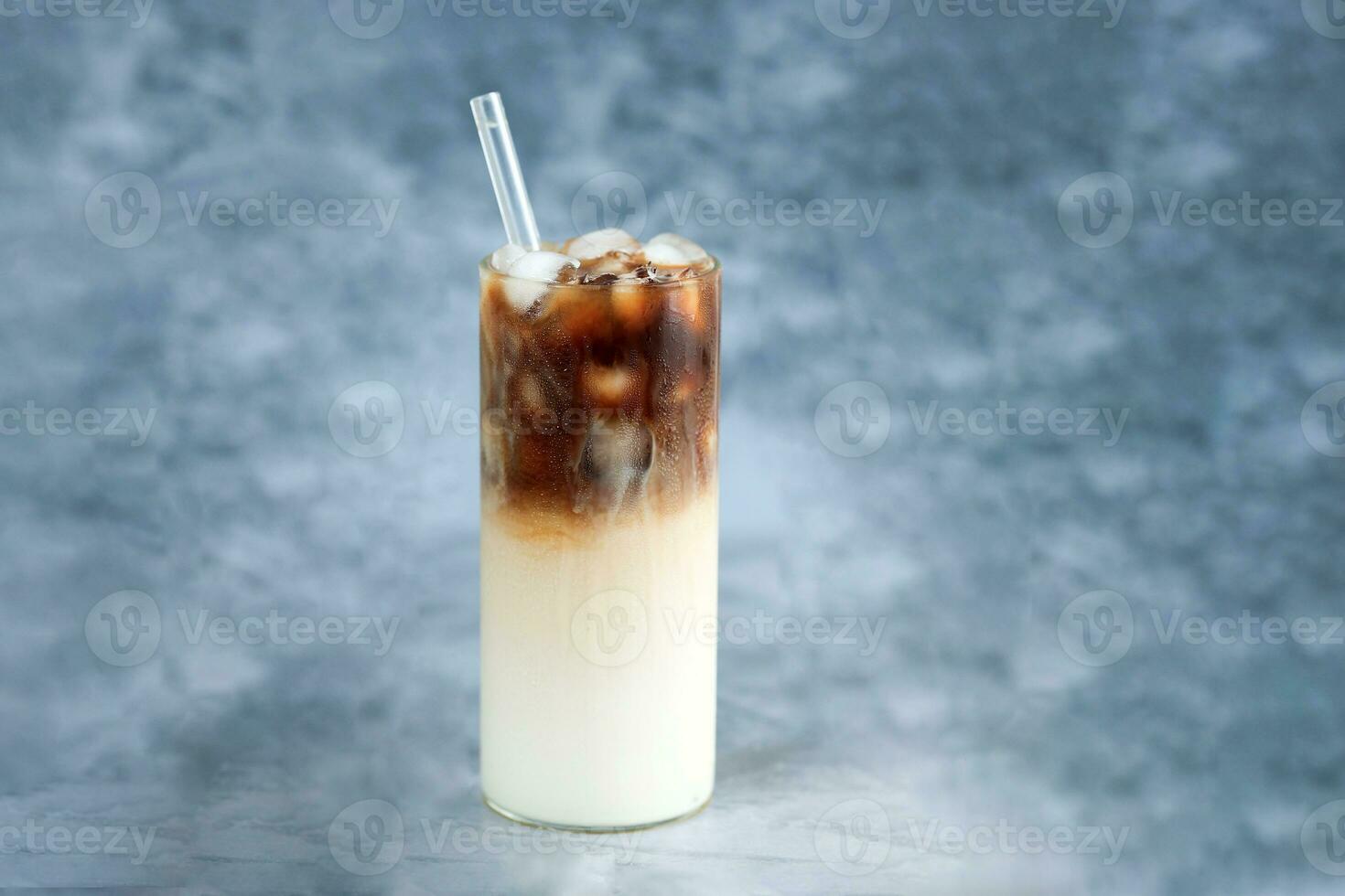 hielo café en alto vaso con vaso paja. hielo cubitos y frijoles en un rústico mesa. foto