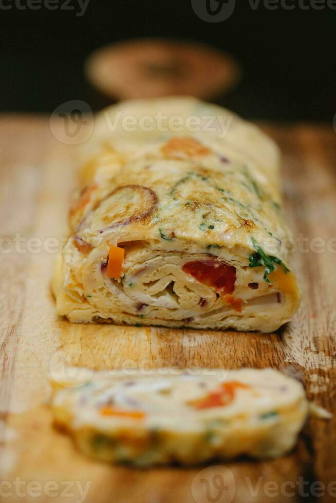 Omelet stuffed with vegetables and cheese on a wooden board. photo