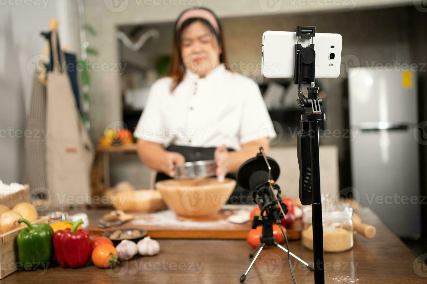 Young attractive Asian woman is blogging for her kitchen channel about homemade pizza while streaming online for webinar masterclass lesson. Vlogger broadcasting live video online teaching cooking photo