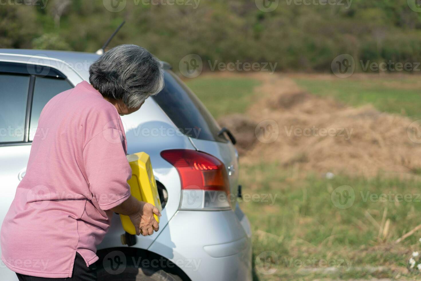 The car ran out of gas and stalled beside the road in suburbs and an elderly Asian woman used a gallon of spare gas to fuel the car. A woman prepares a gallon of spare gas to fuel before traveling. photo