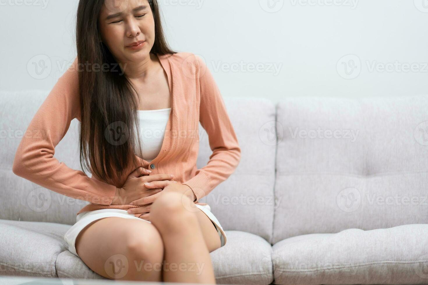 Sick Asian Woman Suffering From Acute Abdominal Pain in the abdomen due to menstruation period, PMS.  Sitting On Couch, stomachache from food poisoning, abdominal pain, digestive problem, gastritis photo