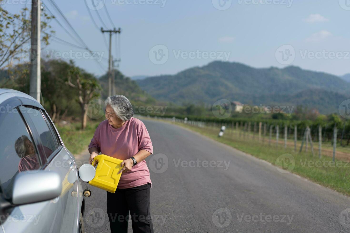 The car ran out of gas and stalled beside the road in suburbs and an elderly Asian woman used a gallon of spare gas to fuel the car. A woman prepares a gallon of spare gas to fuel before traveling. photo