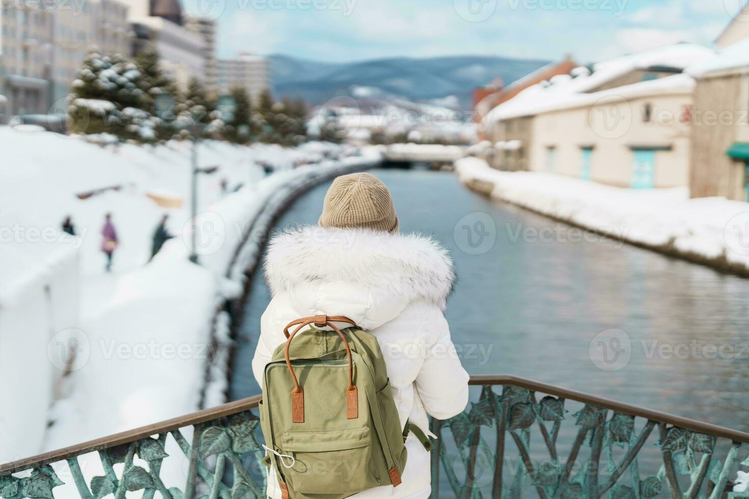 Woman tourist Visiting in Otaru, happy Traveler in Sweater sightseeing Otaru canal with Snow in winter season. landmark and popular for attractions in Hokkaido, Japan. Travel and Vacation concept photo