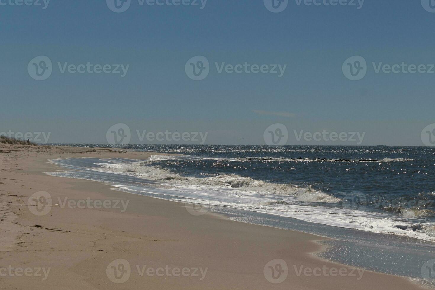 This beautiful beach image was taken at Cape May New Jersey. It shows the waves rippling into the shore and the pretty brown sand. The blue sky with the little bit of cloud coverage adds to this. photo