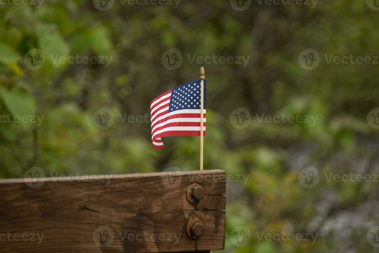 This is an image of a small American flag pinned to a wooden beam. This patriotic display looks quire colorful with the red, white, and blue. The symbol of American is gently flowing in the breeze. photo