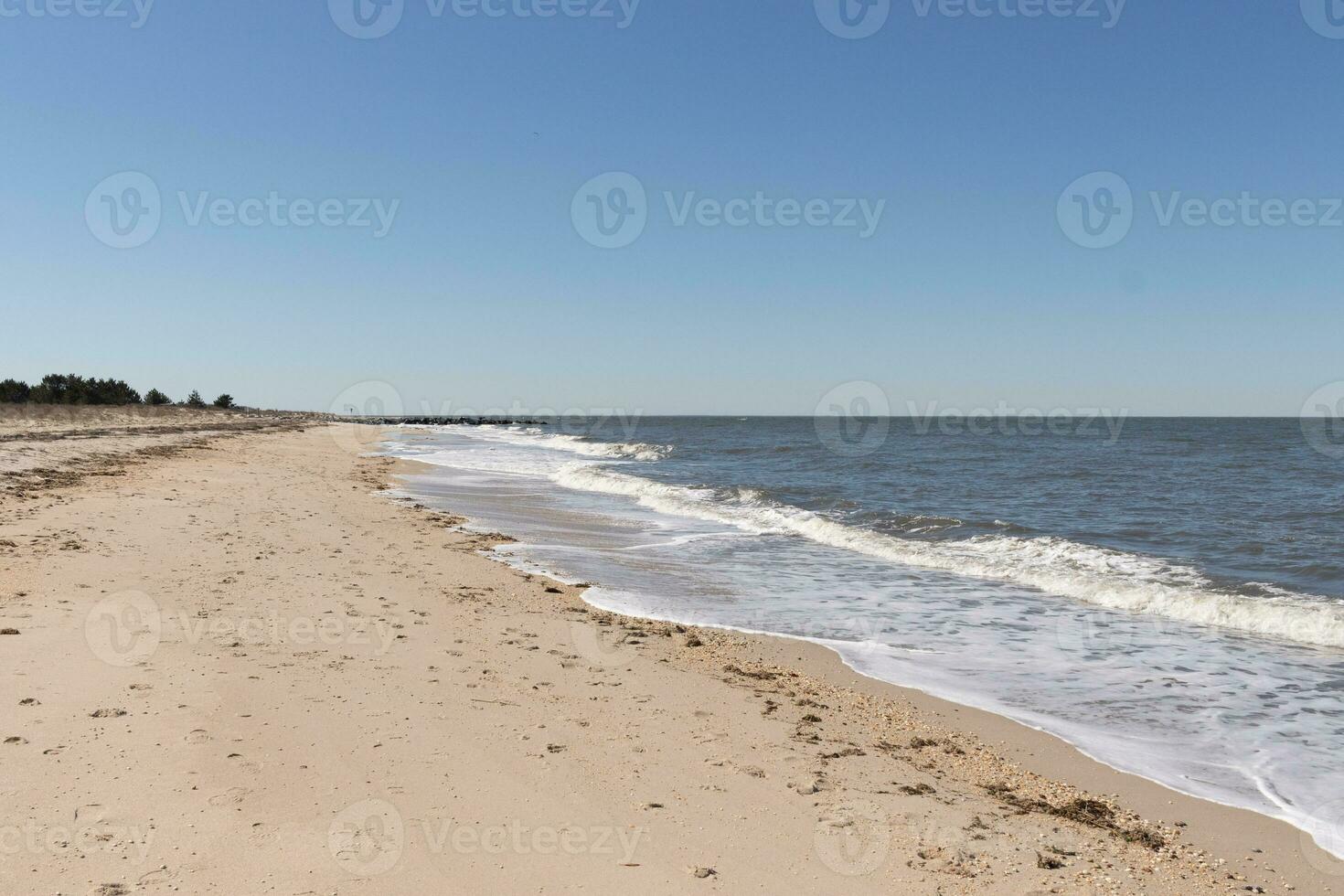 I loved the look of this beach as the waves battered the shore. The whitecaps of the waves make it look rough. The beautiful blue sky with no clouds in site make this look like a beautiful summer day. photo