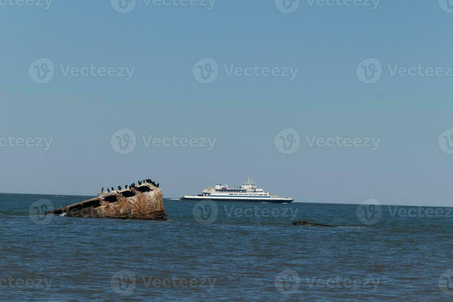 Image taken at Sunset beach in Cape May New Jersey. The sunken ship seen off the coast protruding from the water. The brown rusty hull looking weathered. Cape May Lewes ferry seen passing by. photo