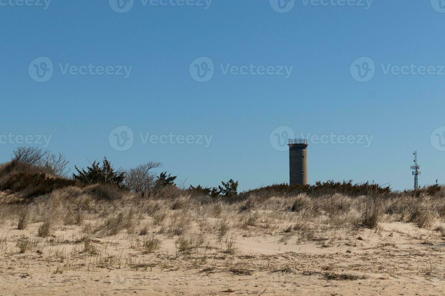 Sunset beach in Cape May New Jersey. The beautiful brown sand all around with tall green grass of the sand dunes. There is a World War II lookout tower in the back. Pretty blue sky in the background. photo