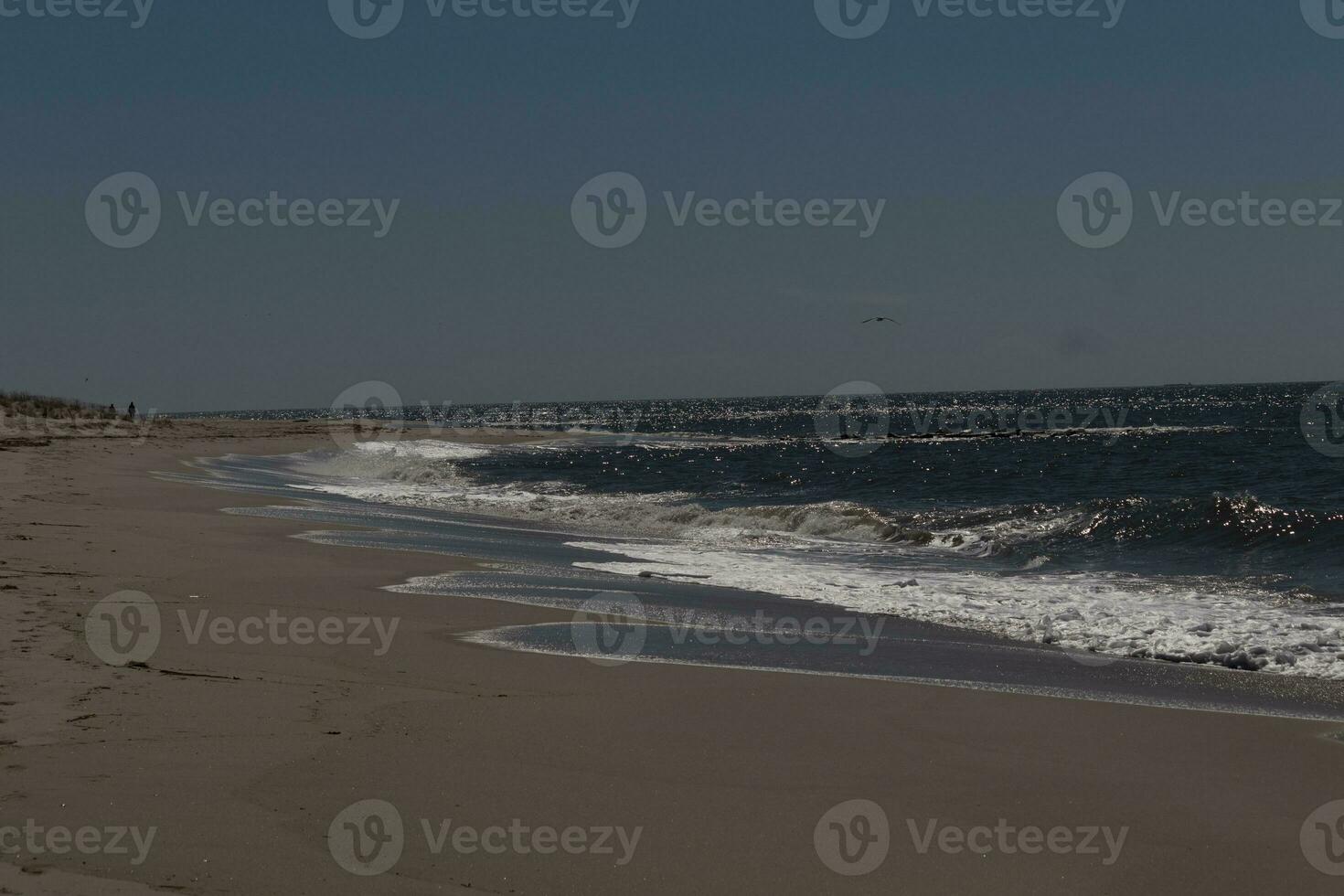 This beautiful beach image was taken at Cape May New Jersey. It shows the waves rippling into the shore and the pretty brown sand. The blue sky with the little bit of cloud coverage adds to this. photo