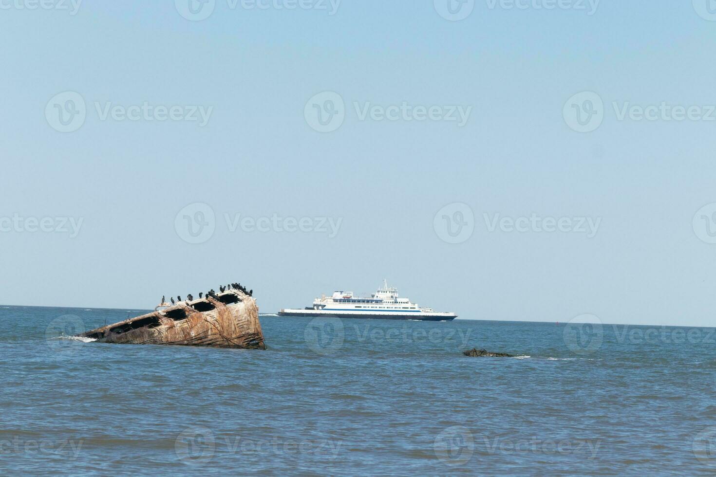 Image taken at Sunset beach in Cape May New Jersey. The sunken ship seen off the coast protruding from the water. The brown rusty hull looking weathered. Cape May Lewes ferry seen passing by. photo