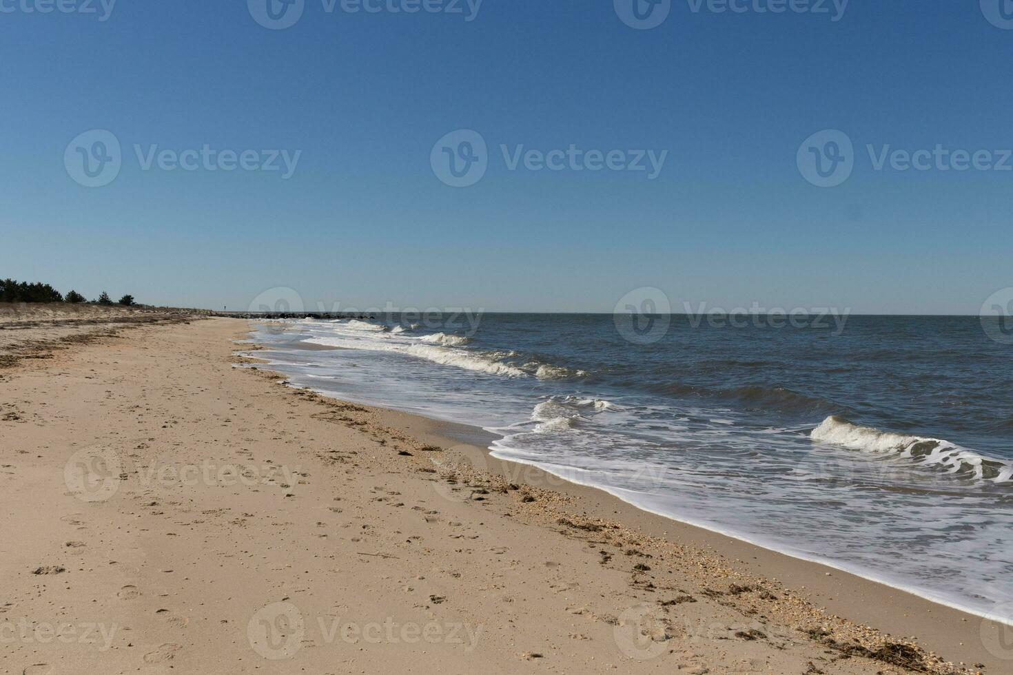 I loved the look of this beach as the waves battered the shore. The whitecaps of the waves make it look rough. The beautiful blue sky with no clouds in site make this look like a beautiful summer day. photo