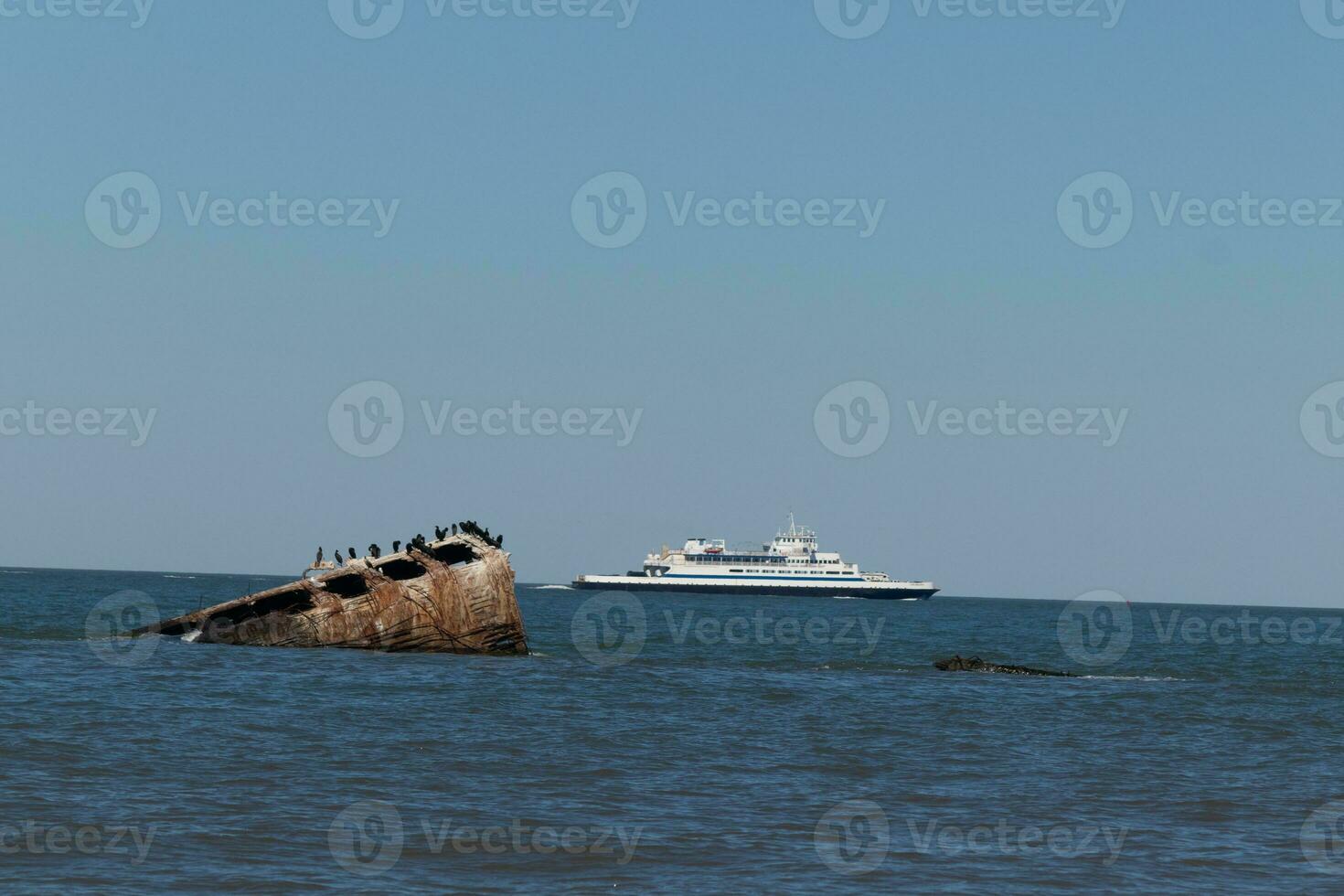Image taken at Sunset beach in Cape May New Jersey. The sunken ship seen off the coast protruding from the water. The brown rusty hull looking weathered. Cape May Lewes ferry seen passing by. photo