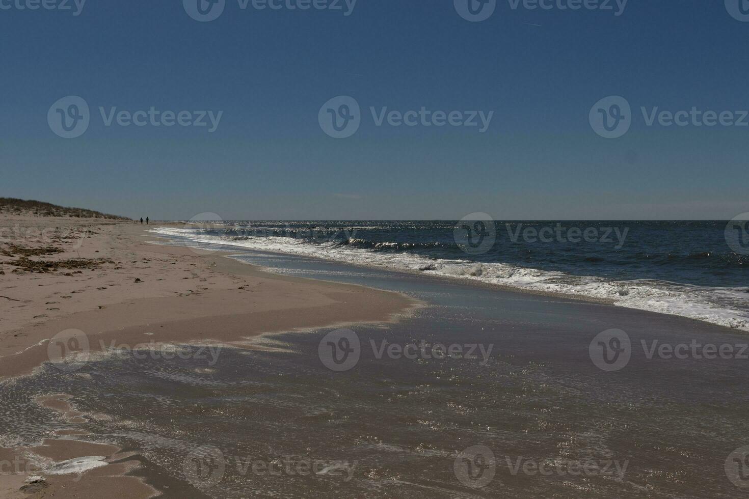 This beautiful beach image was taken at Cape May New Jersey. It shows the waves rippling into the shore and the pretty brown sand. The blue sky with the little bit of cloud coverage adds to this. photo