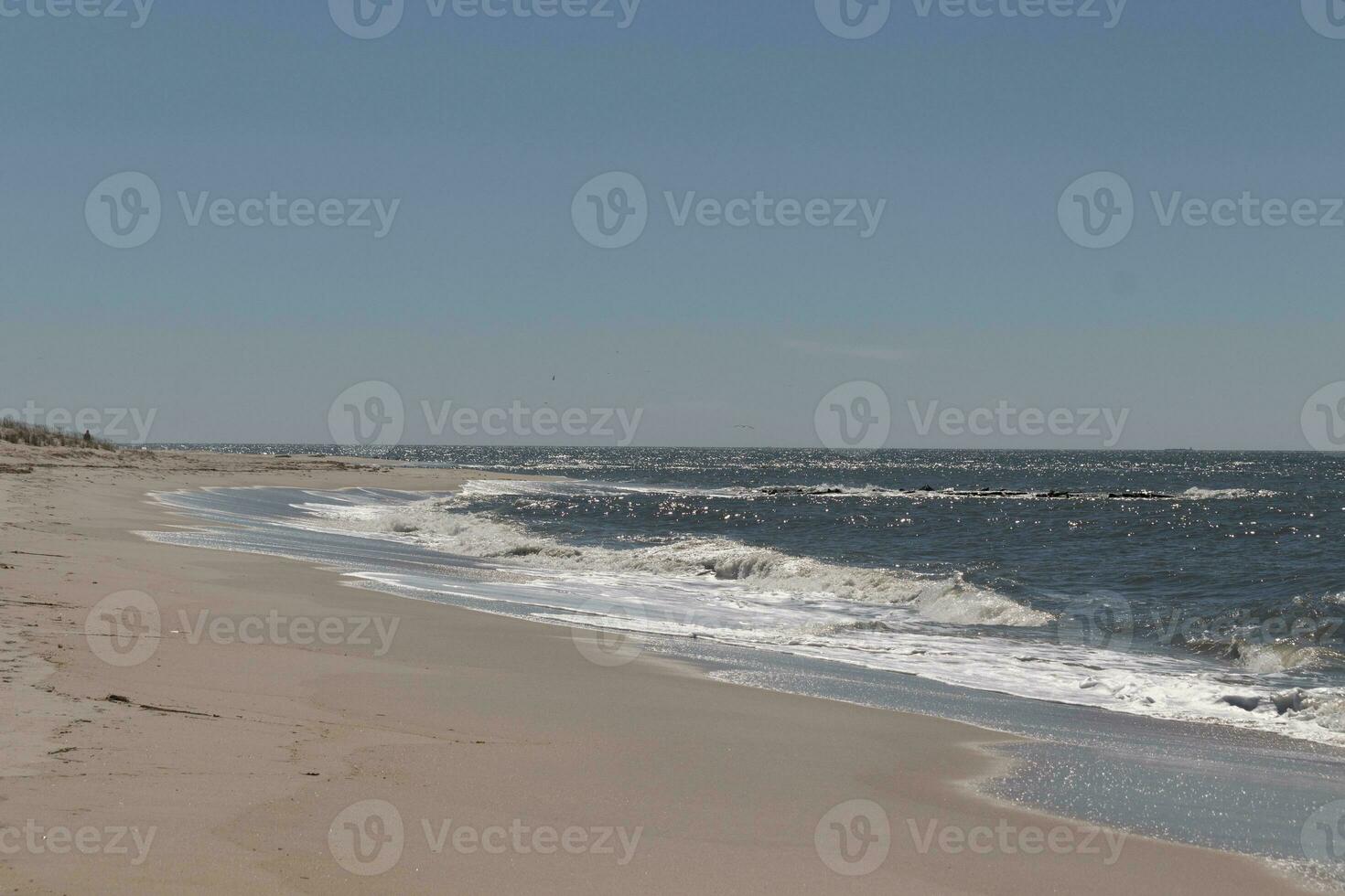 This beautiful beach image was taken at Cape May New Jersey. It shows the waves rippling into the shore and the pretty brown sand. The blue sky with the little bit of cloud coverage adds to this. photo