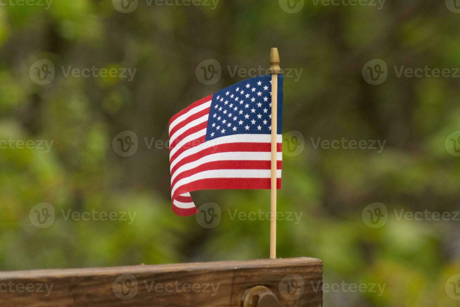 This is an image of a small American flag pinned to a wooden beam. This patriotic display looks quire colorful with the red, white, and blue. The symbol of American is gently flowing in the breeze. photo