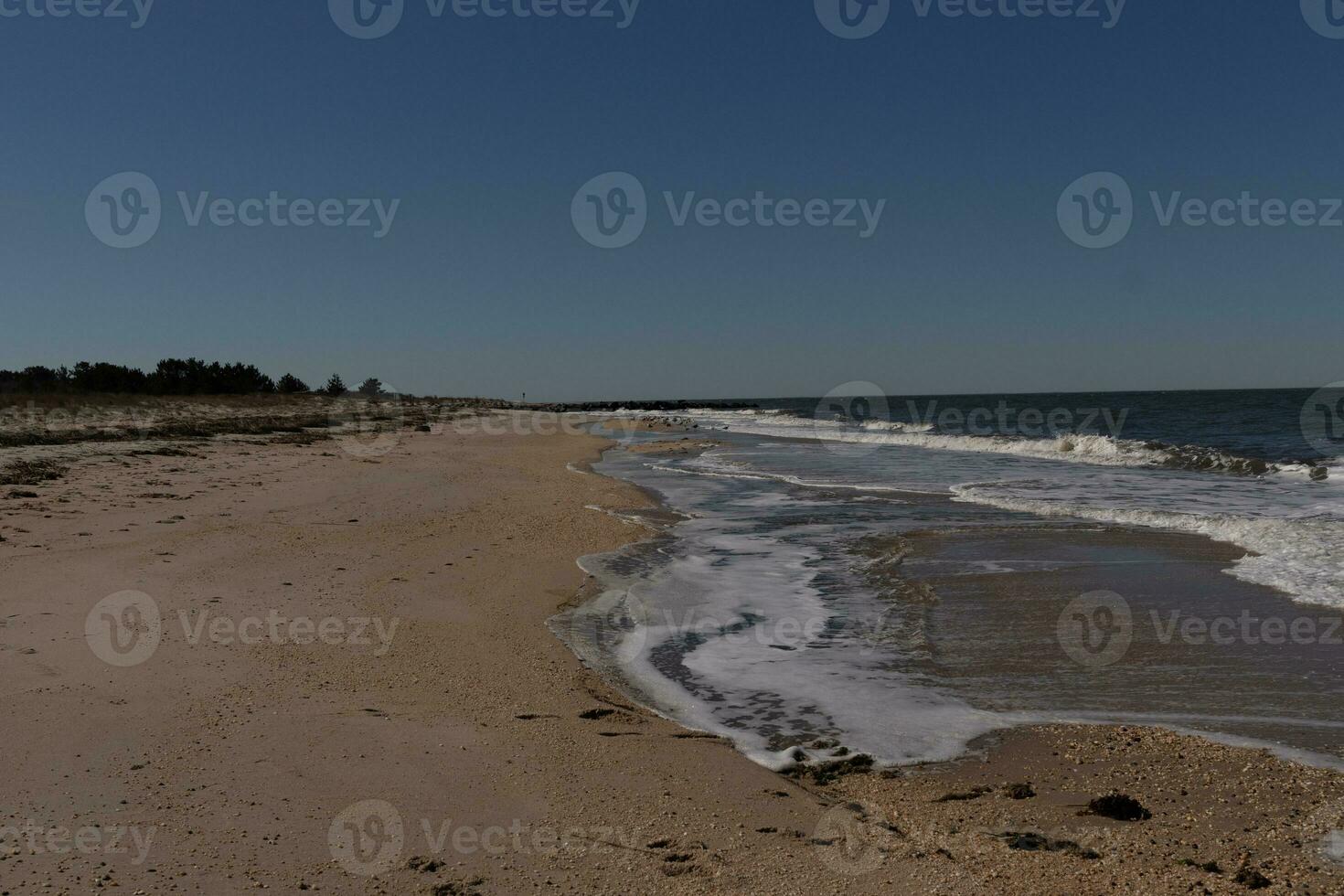 This beautiful image of the surf coming into the beach. The blue ocean with whitecaps on the waves. The water is pummeling the pretty brown sand. The sky is clear with hardly any clouds. photo