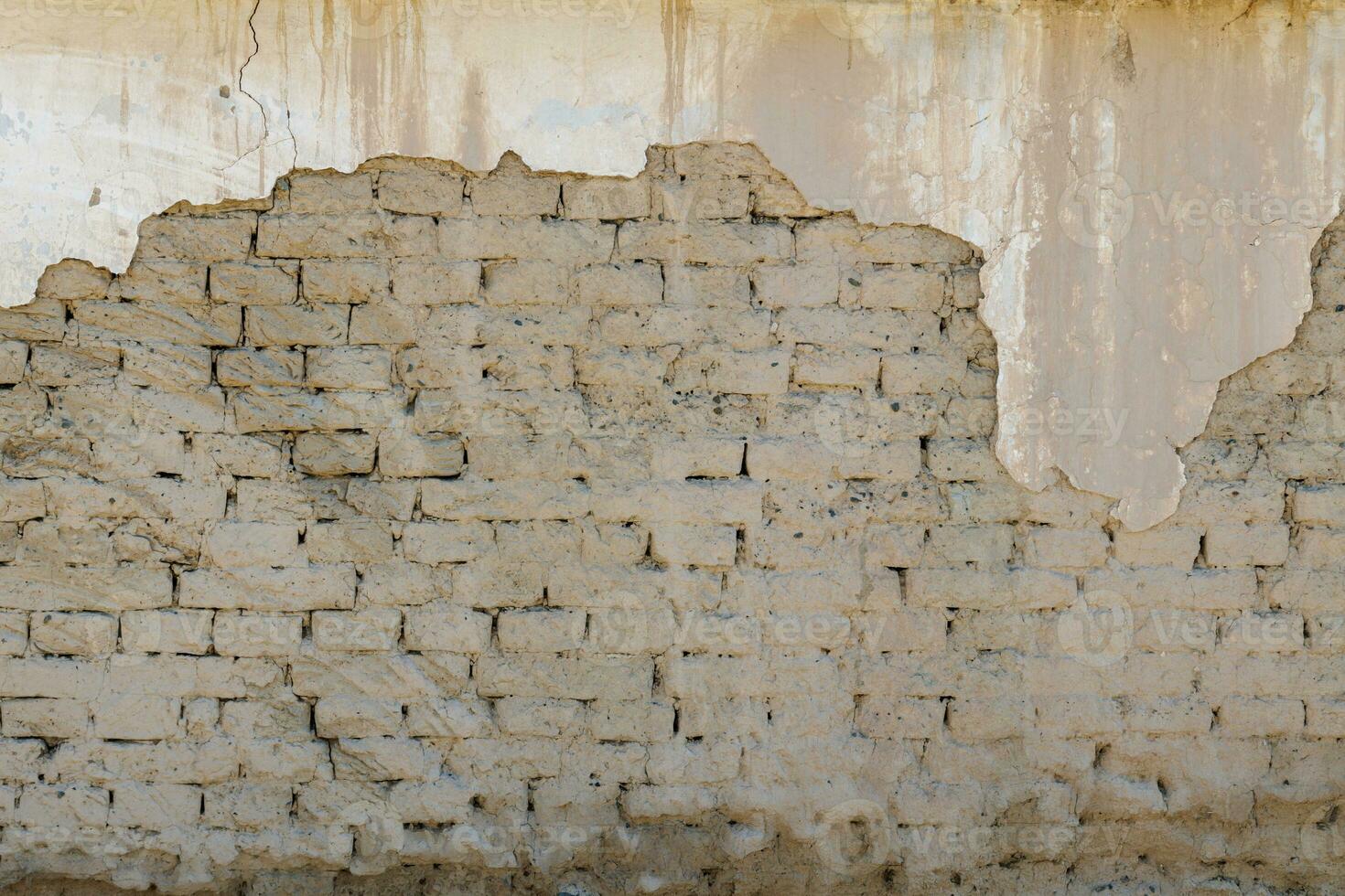 old adobe building wall with peeled off plaster photo