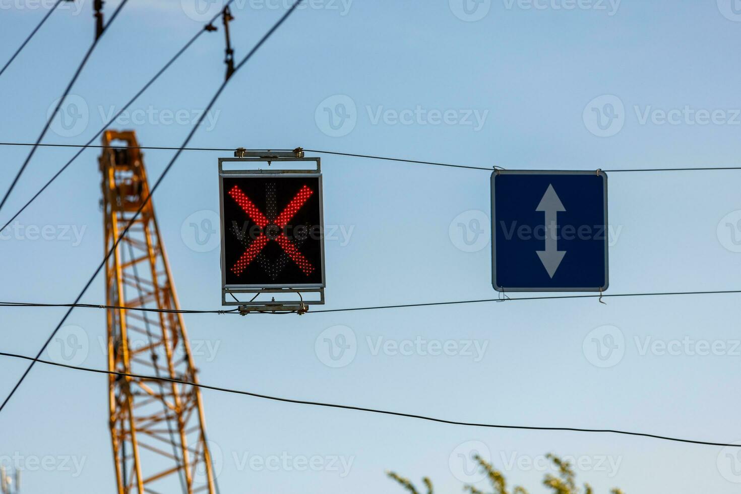 red X light and reversible lane sign above road wtih blurry yellow crane in the background photo