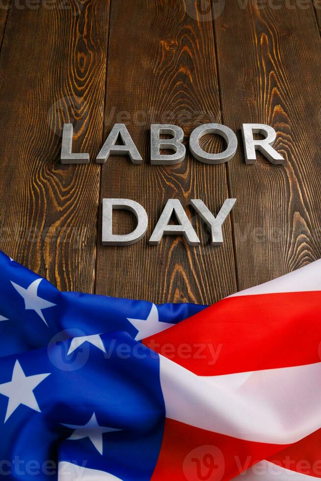 words labor day laid with silver metal letters on wooden surface with crumpled USA flag on bottom side photo