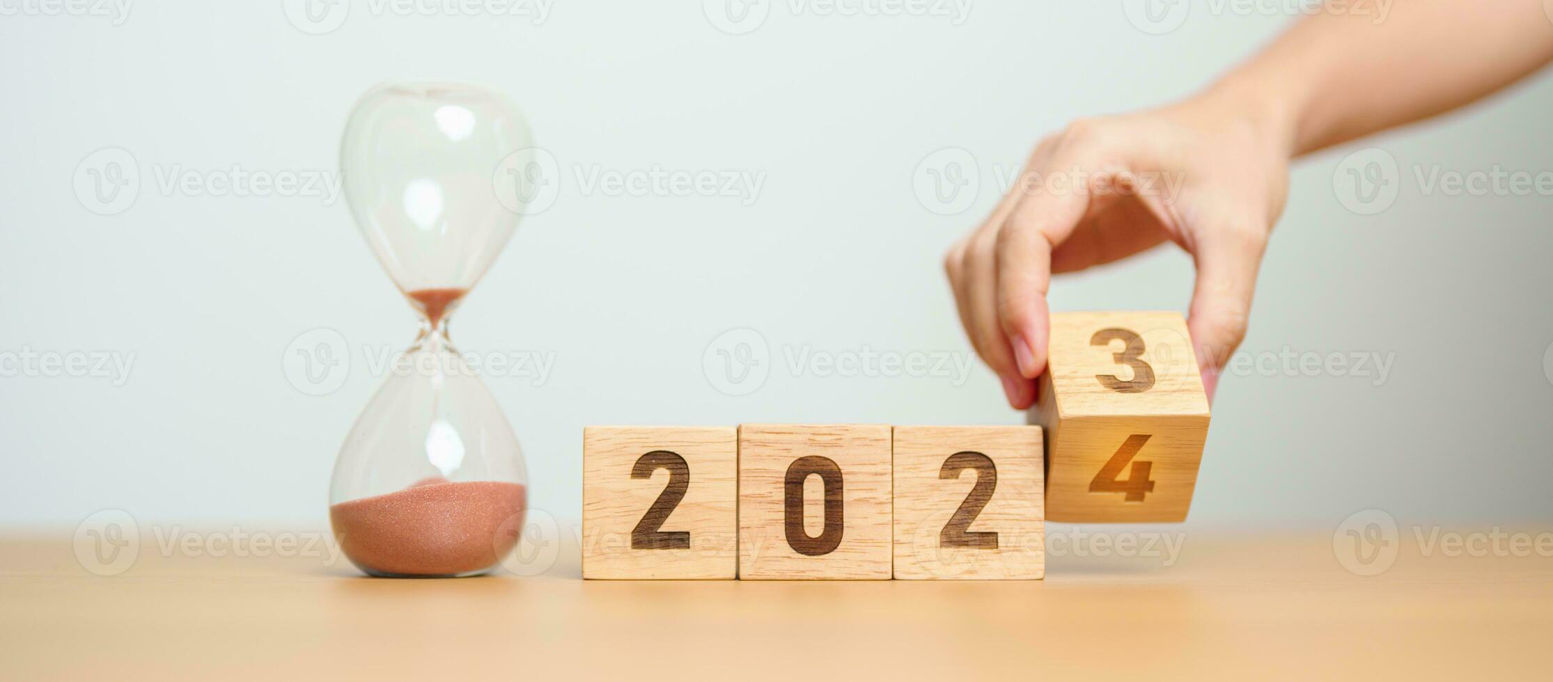 hand flipping block 2023 to 2024 text with hourglass on table. Resolution, time, plan, goal, motivation, reboot, countdown  and New Year holiday concepts photo