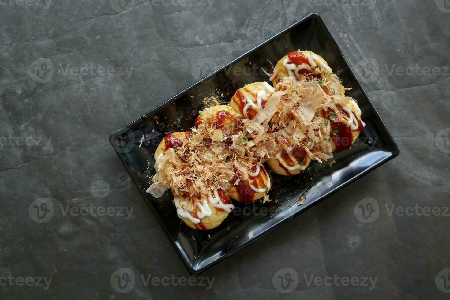 Takoyaki is a Japanese food, made from wheat flour dough, octopus meat, or other fillings, served with sauce, mayonnaise and topping in the form of katsuobushi or wood fish shavings. photo