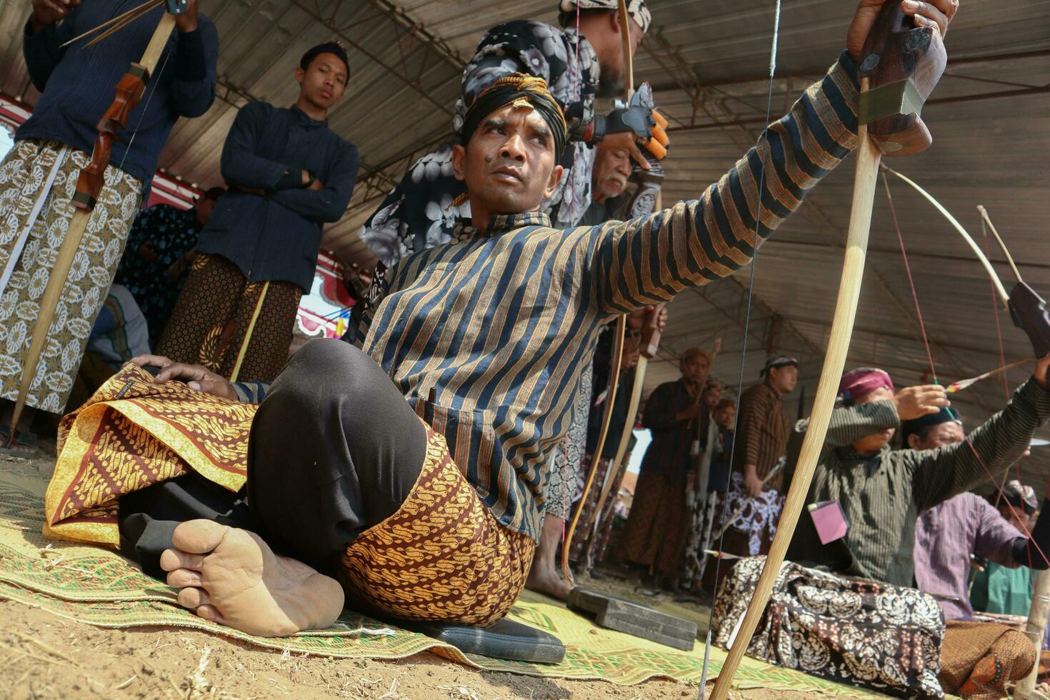 Klaten, Indonesia, august 15, 2023. male and female participants, dressed in Javanese custom pulled his bow by squinting to achieve concentration of target accuracy in traditional Javanese arrow trad. photo