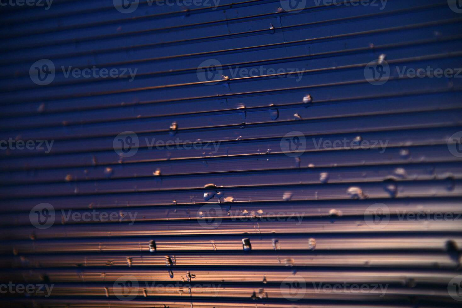 Blue-purple polycarbonate with raindrops. View of wet glass in the setting sun. photo