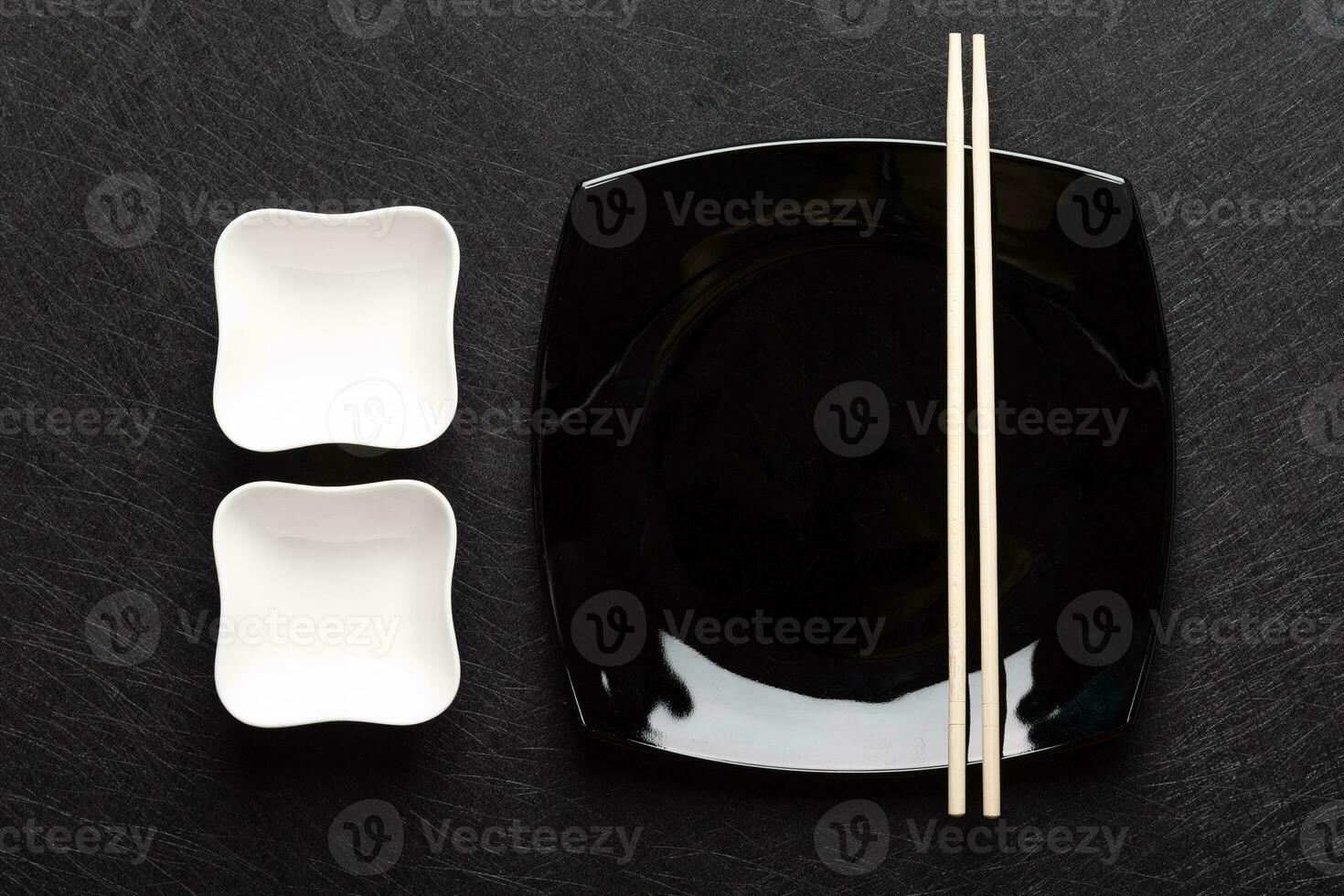 Empty black plate with chopsticks and two white gravy boats on a dark background. Japanese food style. Top view photo