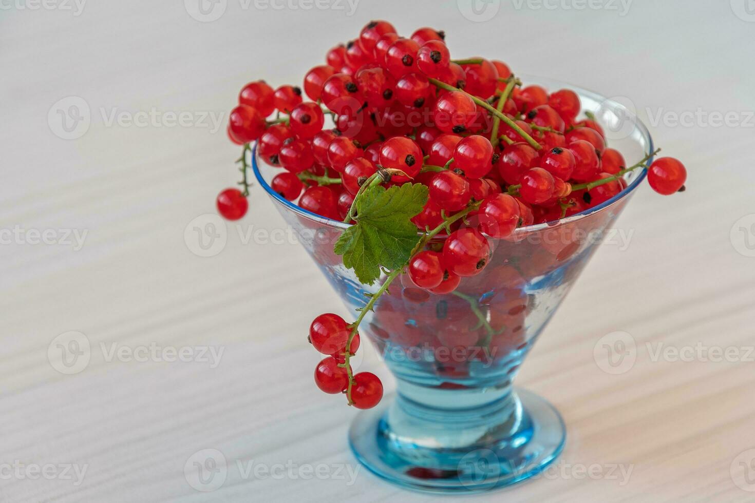 Red currant closeup on twigs in a transparent vase on a light wooden table photo