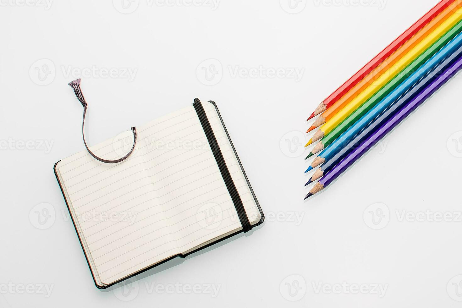 Clean notepad and rainbow color pencils in the shape of an arrow on a white background top view photo