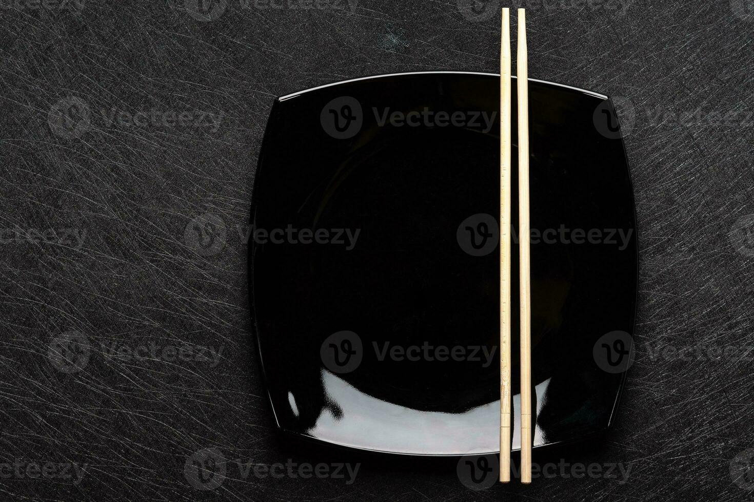 Empty black plate with chopsticks on dark background. Japanese food style. Top view with copy space photo