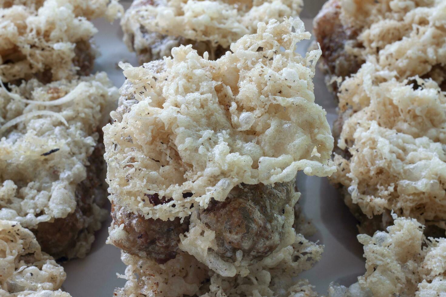 Thai dessert Khao mao tod. Battered and deep fried unripe rice and grated coconut banana rolls on white blotting paper oil. photo